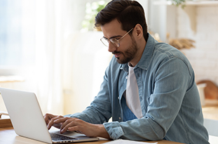 Man sitting at a desk, working remotely on his laptop
